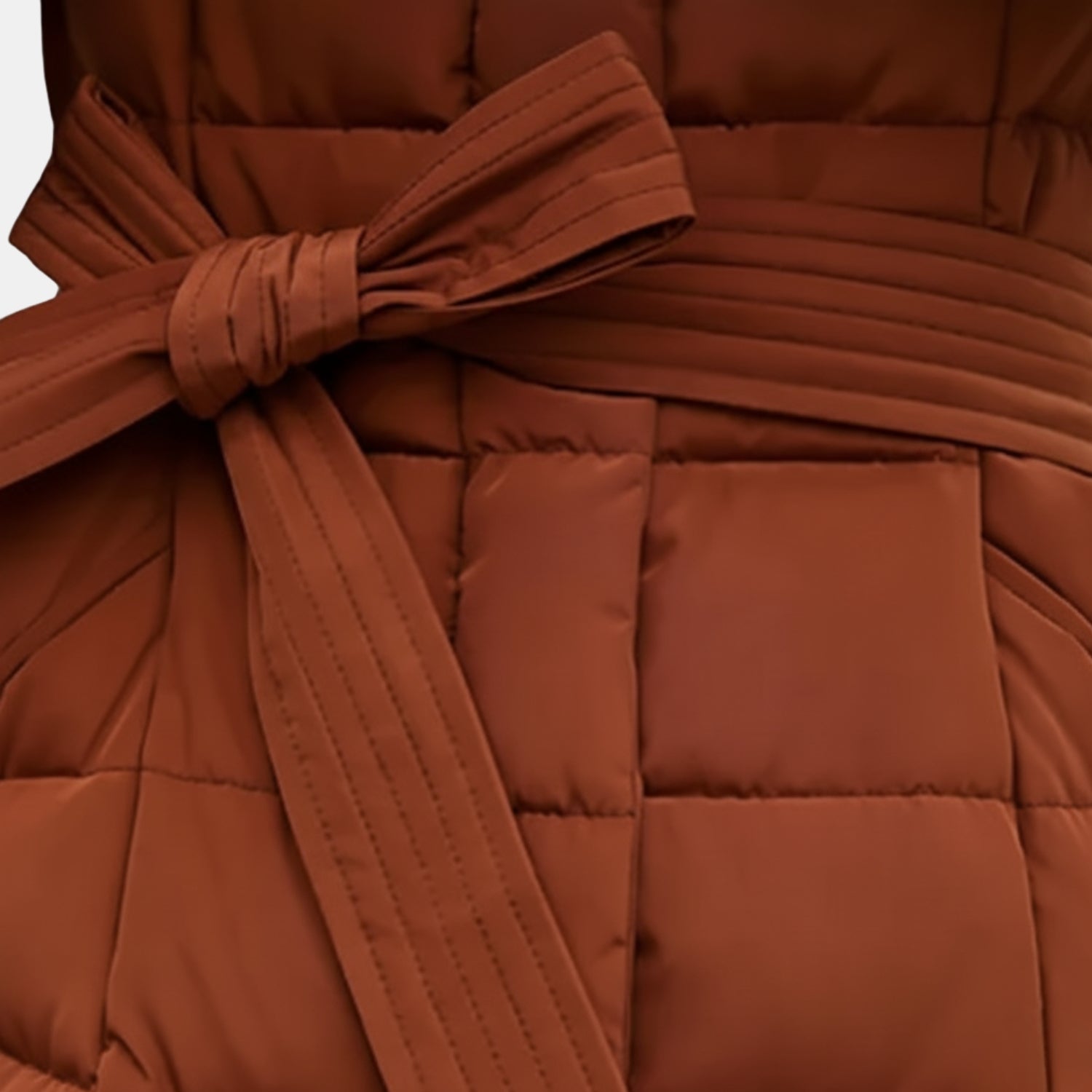 Detailansicht des warmen, bauschigen Wintermantels für Damen in Rostbraun – Nahaufnahme des Taillengürtels und der gestepp­ten Struktur